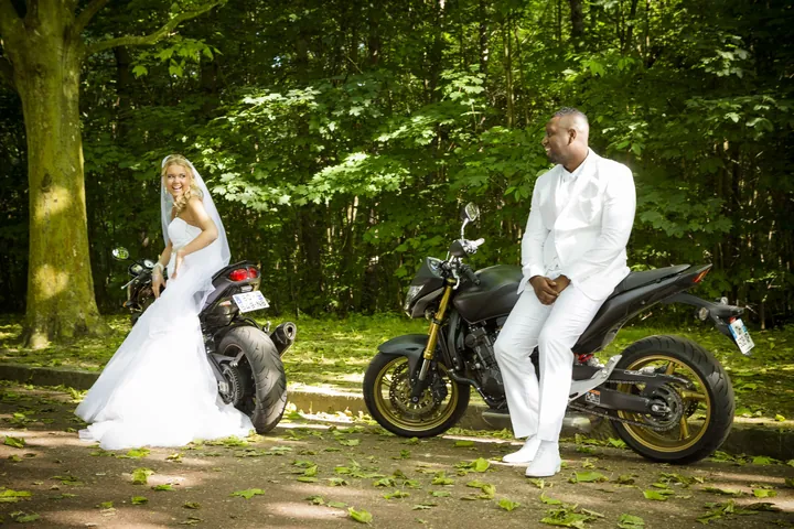 Marié en costume blanc sur une moto, mariée à ses côtés, en forêt